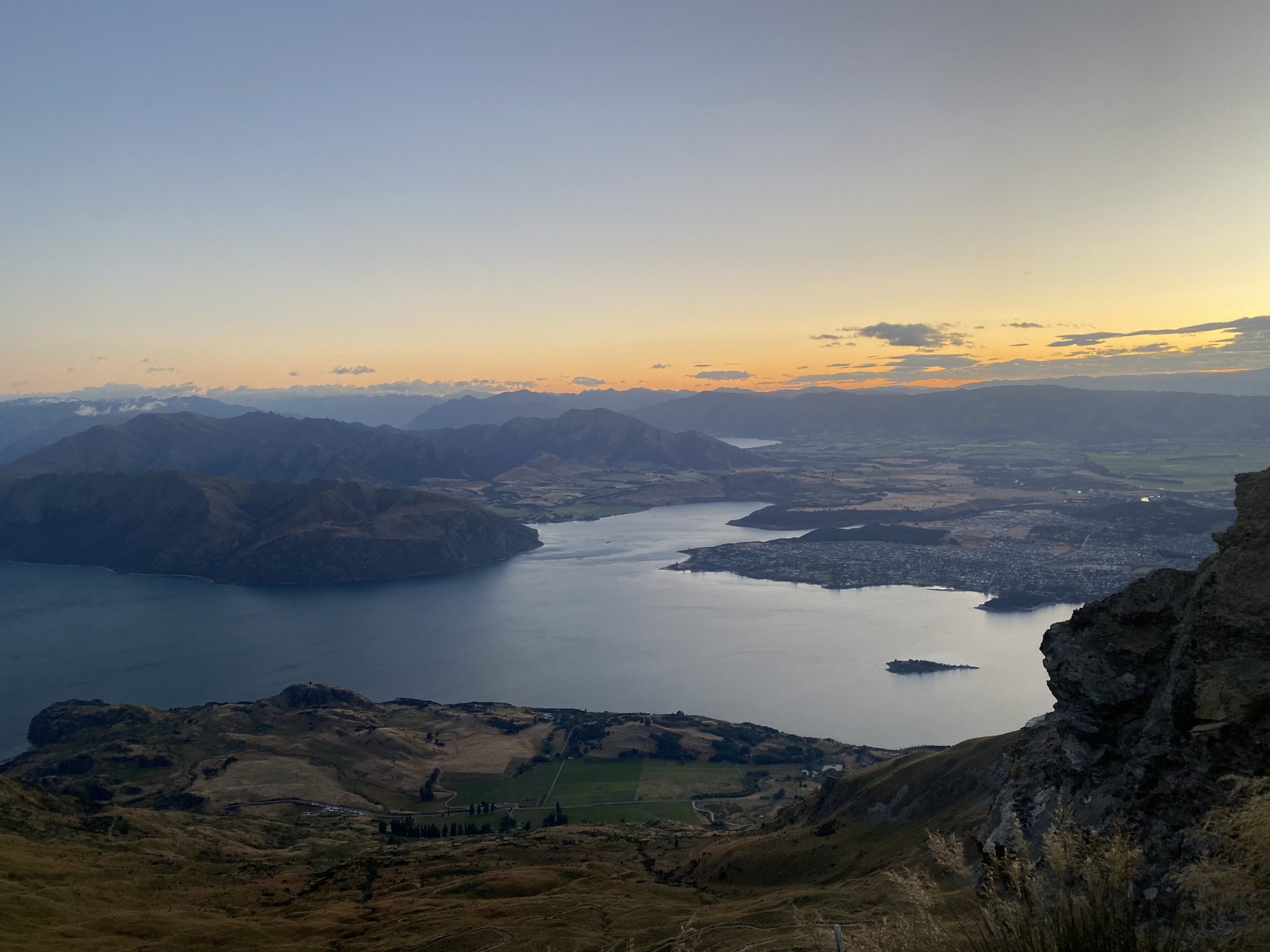 Sonnenaufgang am Roy’s Peak mit Blick über den Lake Wānaka und die umliegenden Berge in Neuseeland.